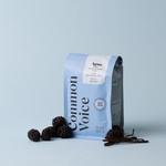 Agua coffee bag on a blue background with blackberries and vanilla beans next to it. 