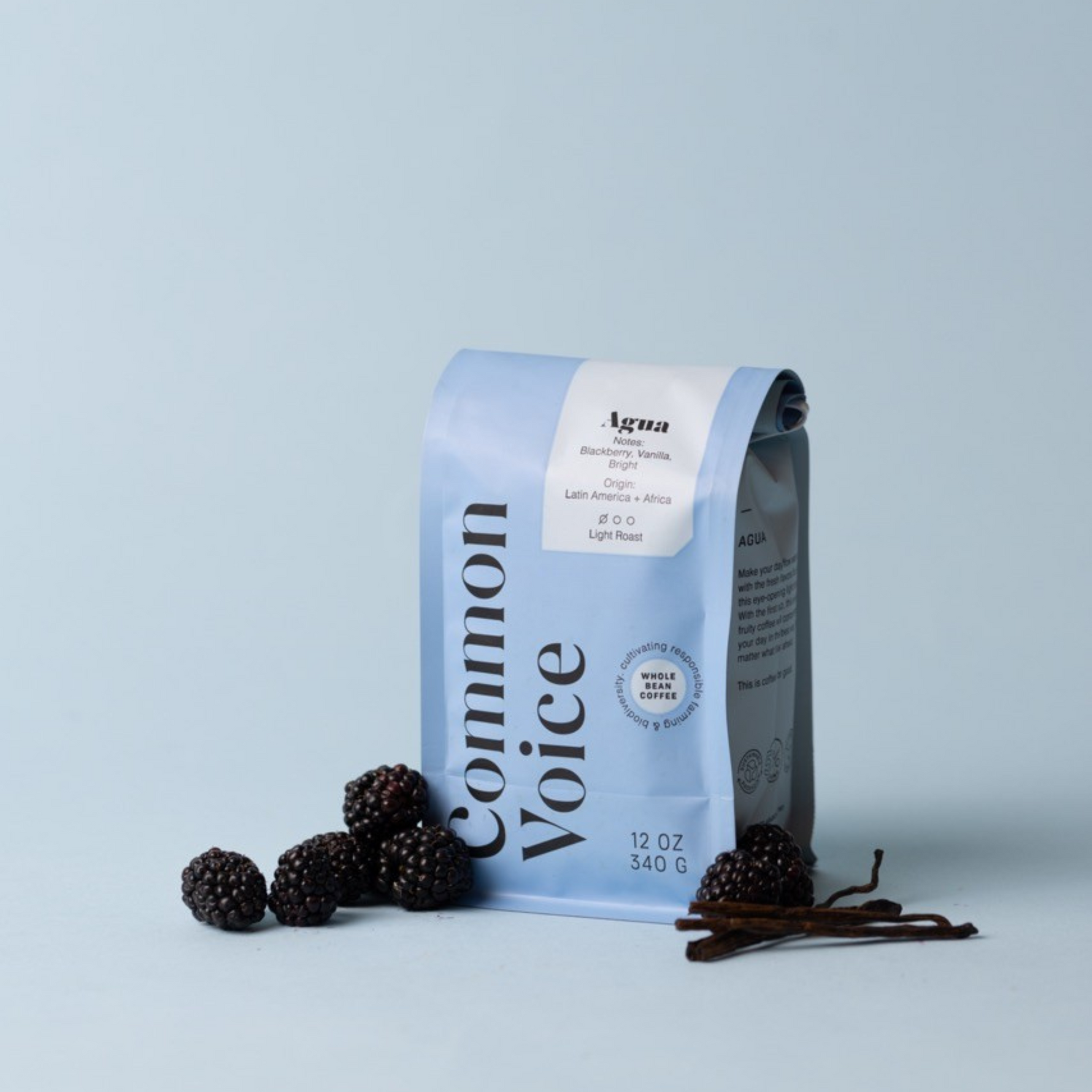 Agua coffee bag on a blue background with blackberries and vanilla beans next to it. 